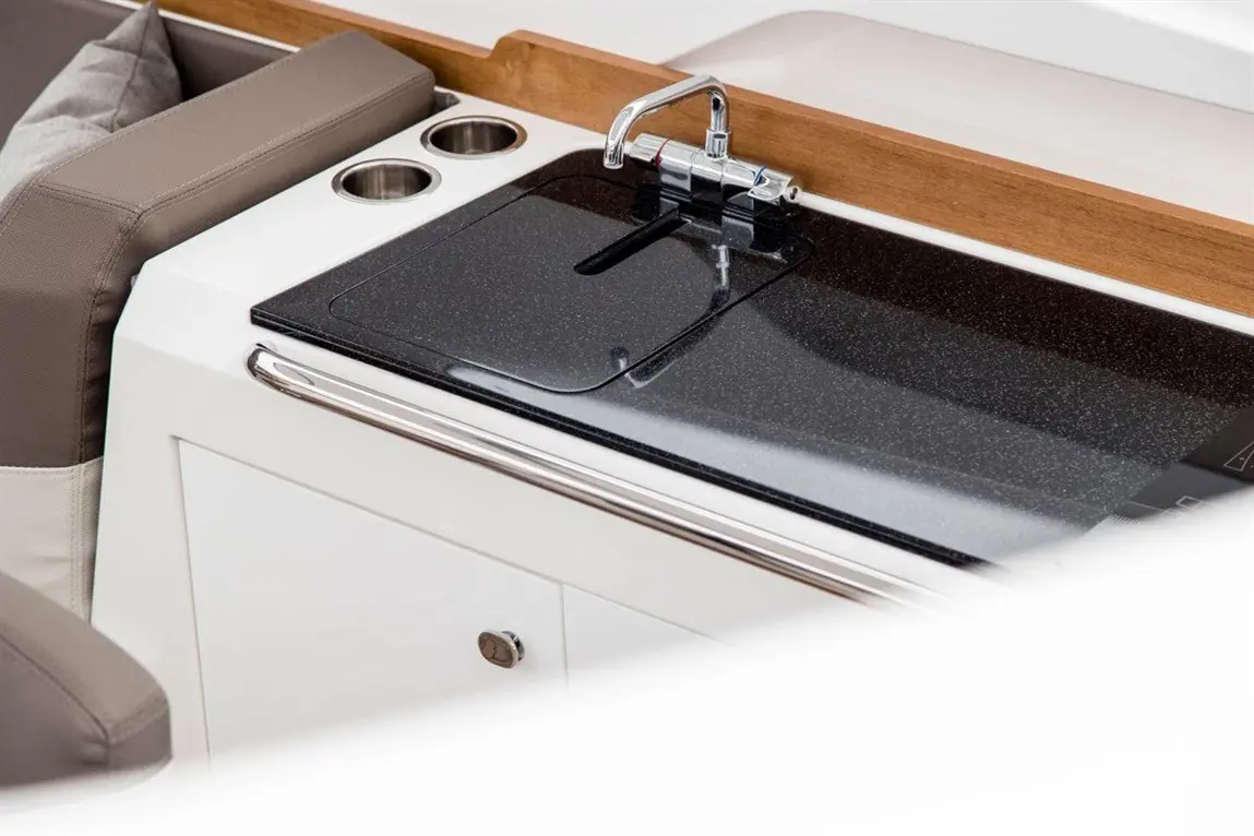 Modern kitchen area on a boat featuring a sleek black countertop, a tap, and two cup holders.